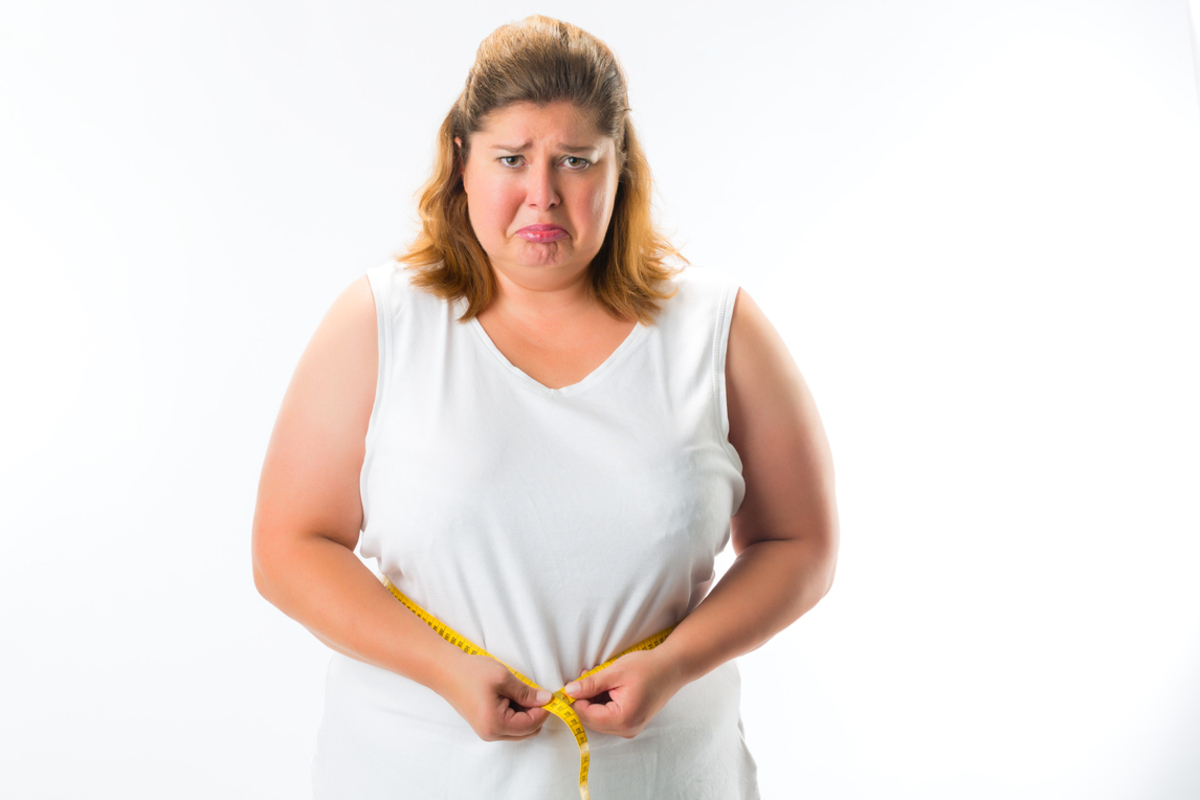  A woman looking sadly at the measuring tape around her waist, symbolizing the challenges and barriers in weight loss.